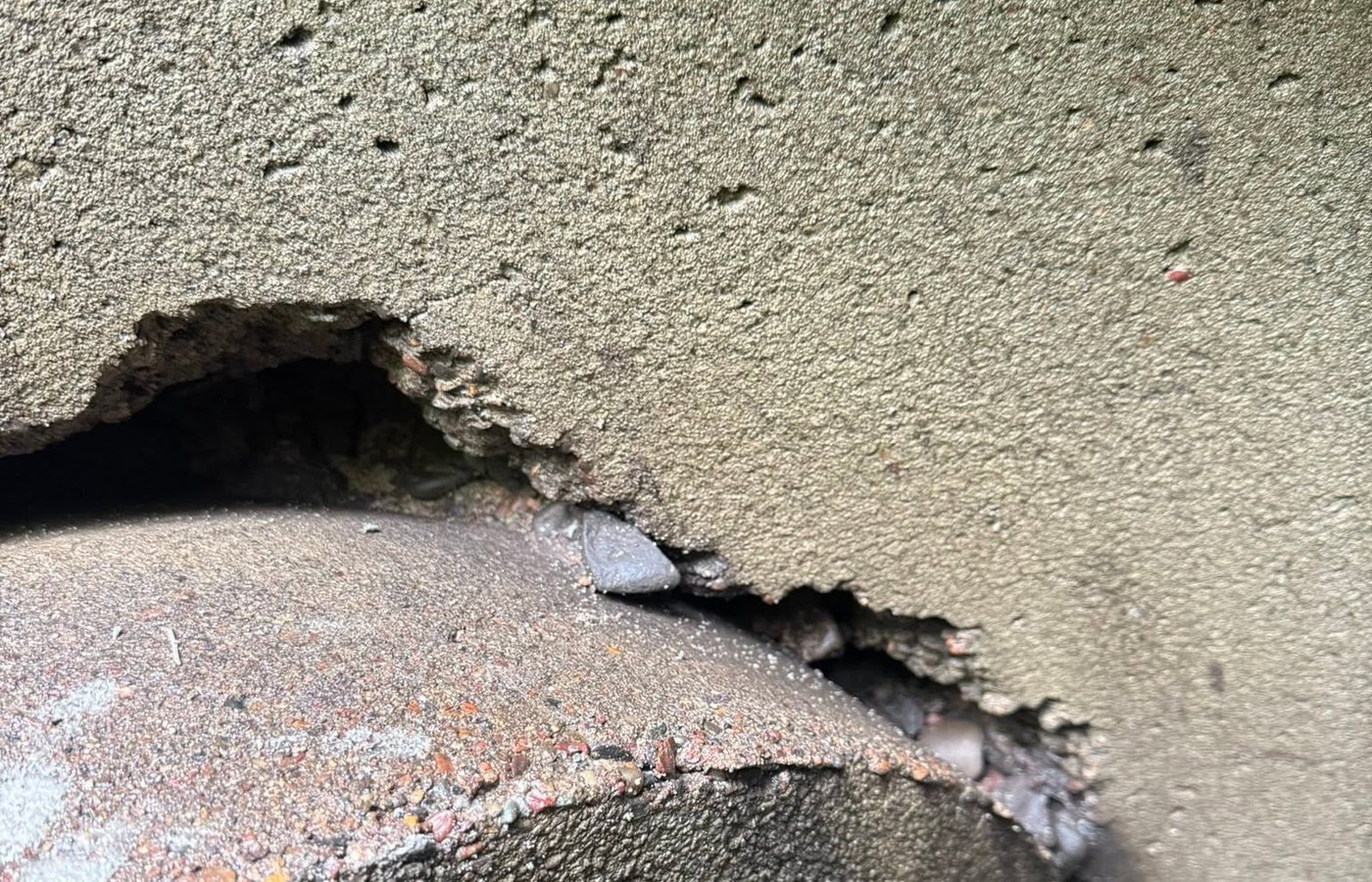 A close view of a catch basin edge where the concrete has broken away and undermined the surface around the grate