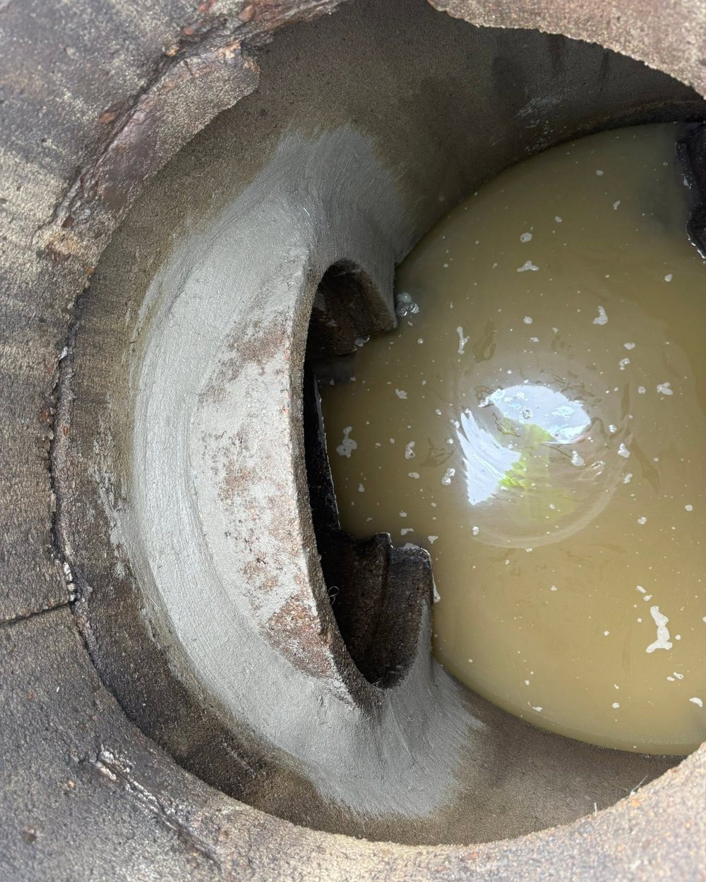 Looking down into a catch basin where the mortar has washed out and water stands in the bottom