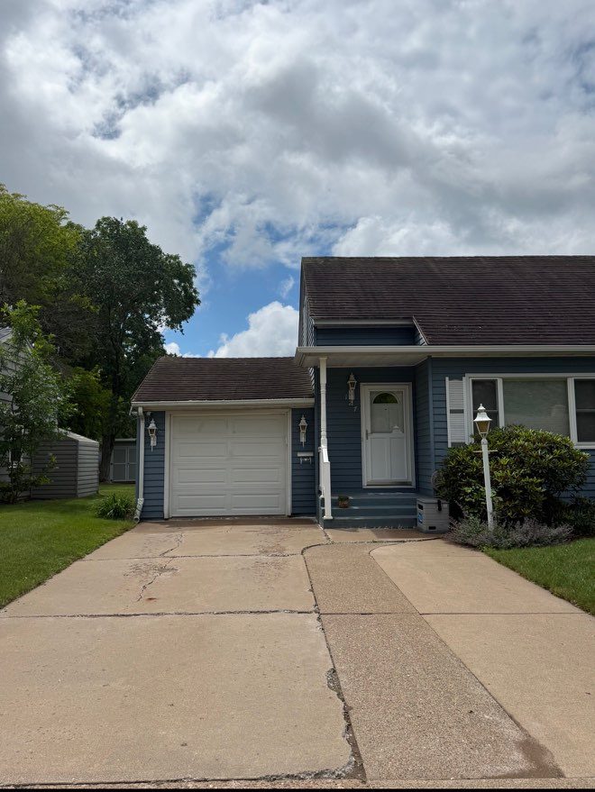 A cracked and patched concrete driveway at a blue house before replacement