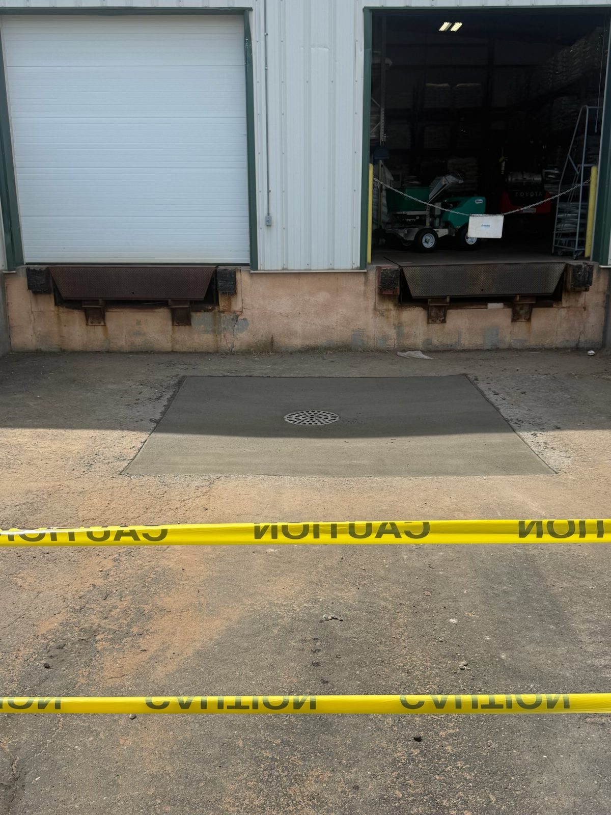 A poured concrete pad around a drain grate at the foot of two loading dock doors