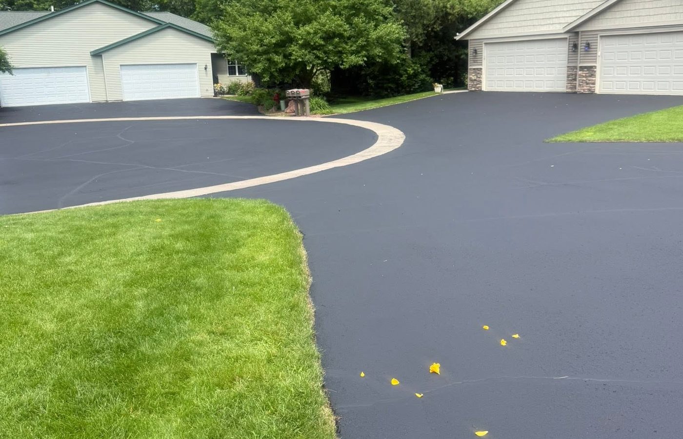 A freshly sealcoated shared court between garages, a concrete walkway curving through it
