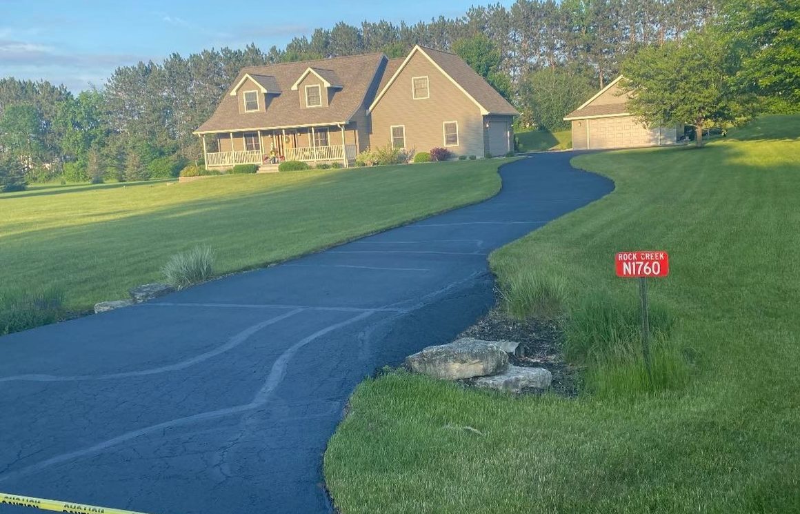 A freshly sealcoated driveway winding up to a house in evening light