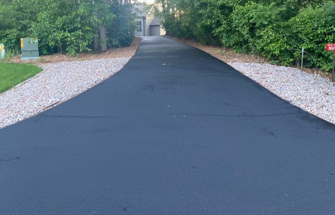 A freshly sealcoated driveway running through the woods, caution tape across the entrance