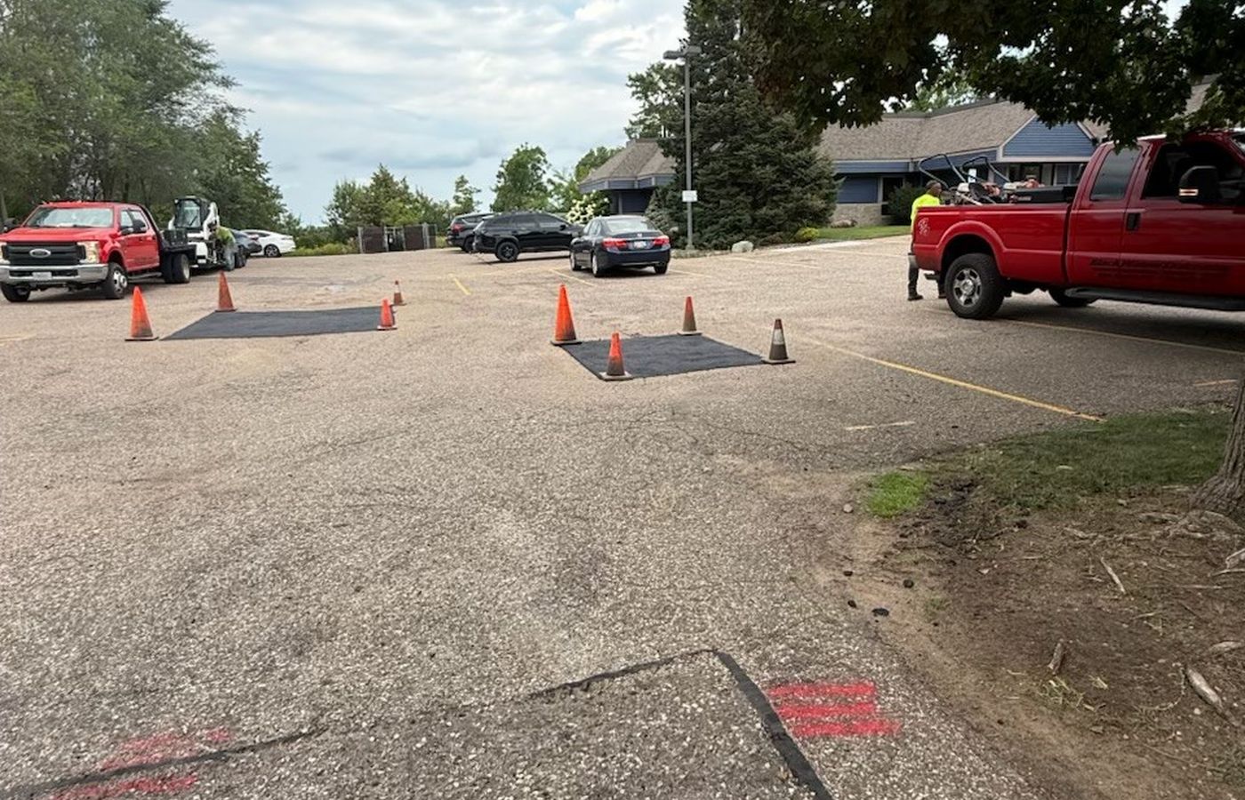 Fresh asphalt patches laid into a parking lot, work area coned off
