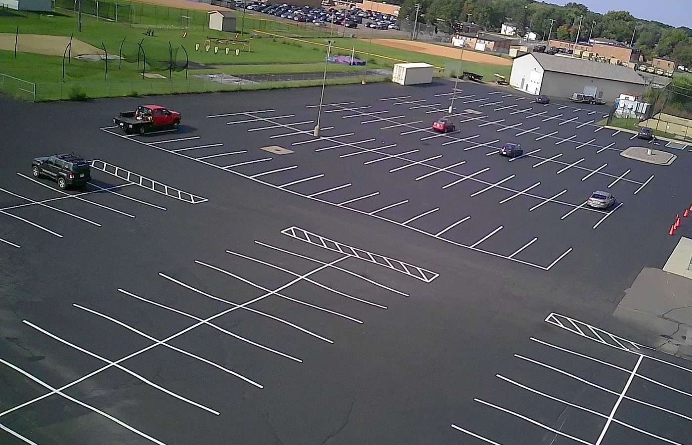 A freshly sealed and striped commercial lot from above, the company flatbed parked on it