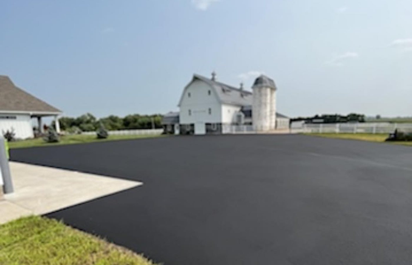 A freshly paved asphalt driveway running up to a three-bay garage, caution tape across the street end