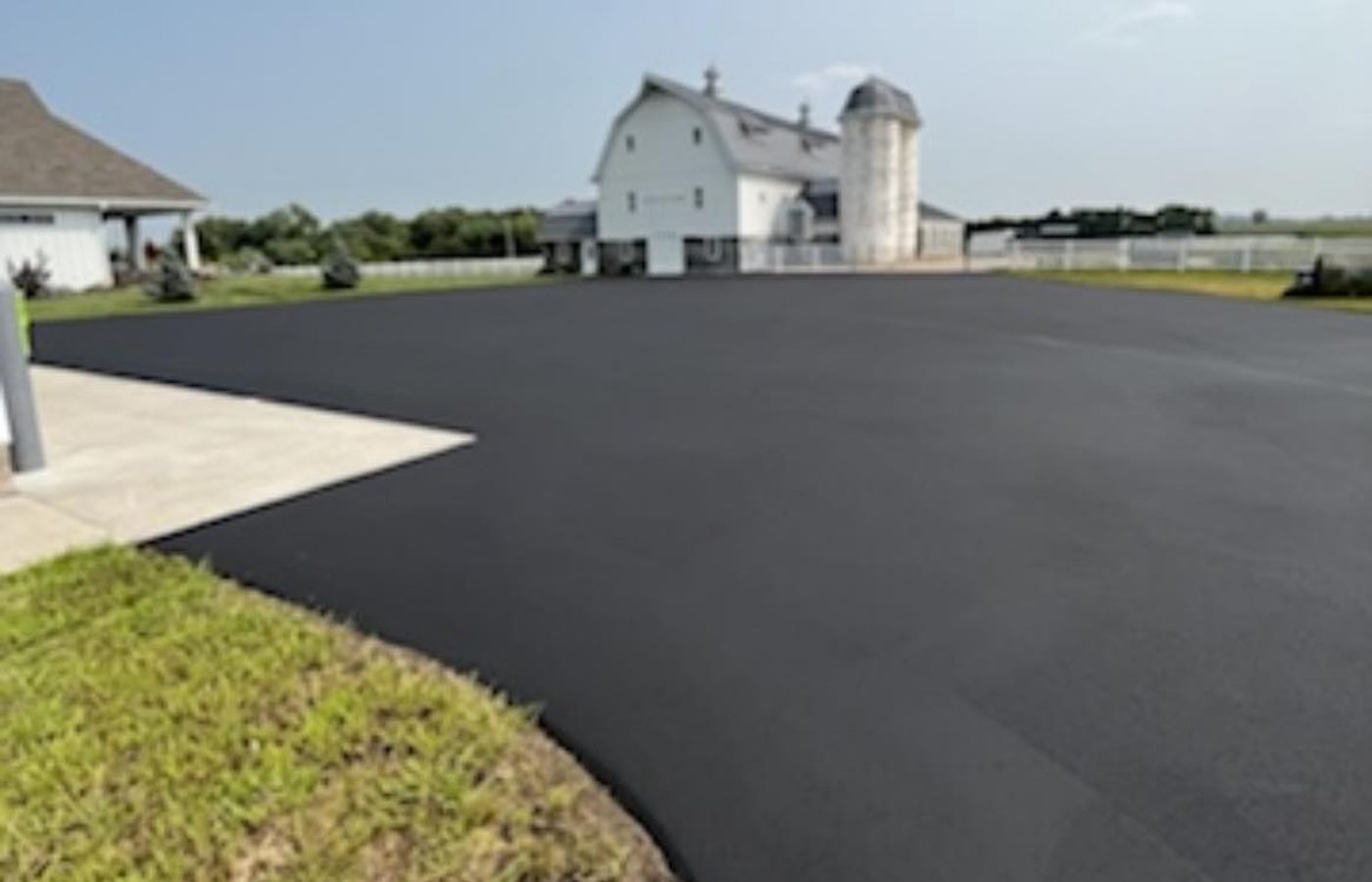A freshly paved asphalt lot in deep black, running up to a white barn and silo.