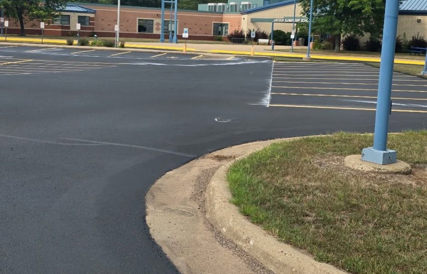 A large freshly paved asphalt lot curving around a landscaped island in front of a low institutional building