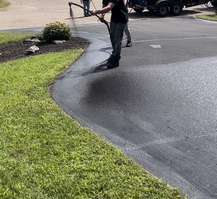 A crew member spray-wanding sealcoat across a driveway