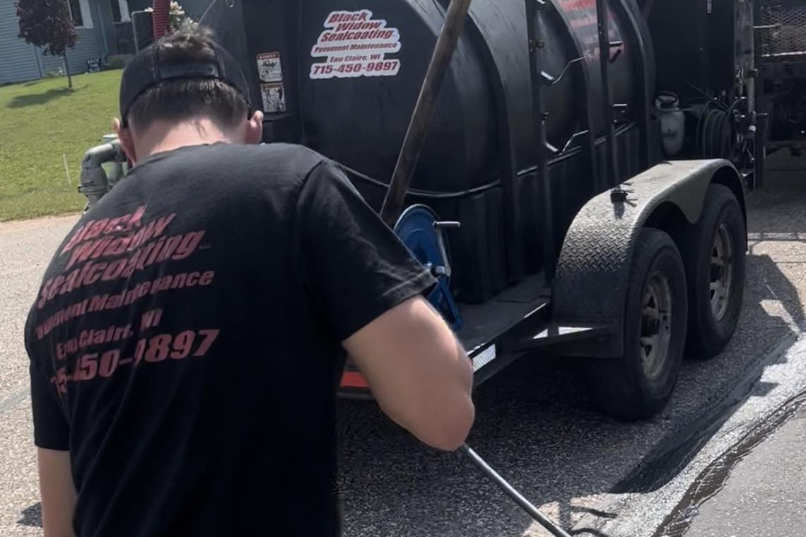 A crew member spraying sealcoat from the black tank rig