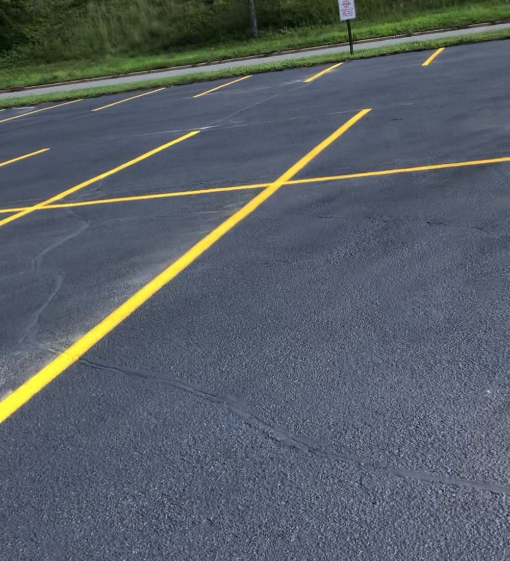 Fresh yellow stall lines crossing a newly sealed parking lot, deep black surface